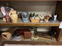 Shelf with various figurines including an elephant, Indian figure, small basket, dogs, cats, and other decorative items on top shelf; wood box, iron, brush and metal mirror on bottom shelf.