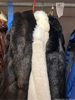 Three faux fur coats and jackets hanging on a rack, white, black and dark brown/black in color.