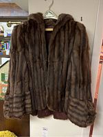 Front view of a brown real fur jacket hanging on a hanger showing vertical fur patterns and plush collar.