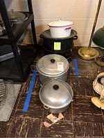 Overview of all pots stacked on the floor including porcelain pot, crab steamer, and aluminum pots.