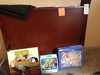 Wooden puzzle board with three 1000-piece jigsaw puzzle boxes arranged in front: Cute Cats, Lighthouse, and County Fair.