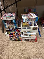 Stack of assorted boxed jigsaw puzzles on carpeted floor including bright colorful gem design and various other themes.