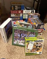 Stack of various 1000-piece puzzle boxes and some with other piece counts including Christmas, cats, mountain, city themes