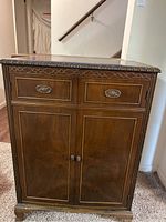 Front view of wood record cabinet showing two drawers with metal handles on top and two doors with round knobs below; decorative carving around the top edge.