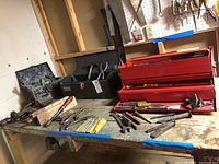 Photo of workbench with two toolboxes (one red ServiStar toolbox with drawers, one dark toolbox), assorted hand tools including hammers, screwdrivers, punches, and vise grips laid out.