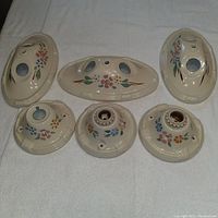 Top-down view of six antique ceramic light socket covers with floral designs, arranged on white cloth.