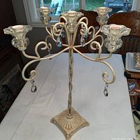 Front view of metal five-arm candelabra with hanging crystal pendants on a white table