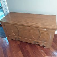 Closed chest showing the arborite finish wood surface with carved detail and brass hardware drawer below.