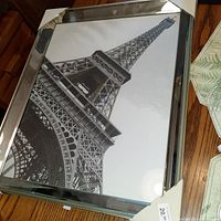 Black and white framed Eiffel Tower picture with reflective metal border, angled view showing frame and photo details.