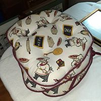 Top view of one fat chef themed round cushion showing fabric pattern and burgundy piping.