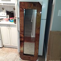 Single tall floor mirror with a dark wood grain frame, rectangular reflective surface. Protective corner covers visible.