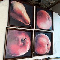 Four framed paintings of fruit arranged in a 2x2 grid on a white surface. Top left is a pear, the other three are different apples.