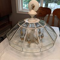 Kitchen light fixture with a white metal base and a large glass geometric shade that encloses four candle-style bulbs.