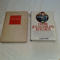 Photo of two hardcover cookbooks laid flat on a surface, one with a patterned box cover (Mastering the Art of French Cooking) and another with a white dust jacket featuring Julia Child (From Julia Child's Kitchen).