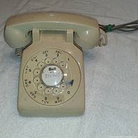 Beige vintage Bell rotary dial telephone with visible numeric and alphabetic dial, handset and cord.