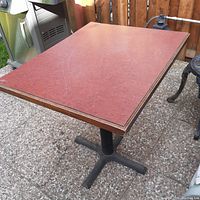 Photo showing red laminate square table top with minor scratches and black metal base on outdoor patio.