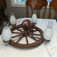 Wagon wheel styled light fixture with four white frosted glass shades laid flat on table showing full item and details.