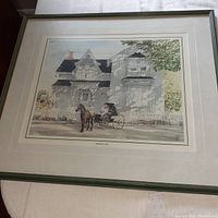 Framed watercolor-style print showing a horse and carriage in front of a large house with a white picket fence.