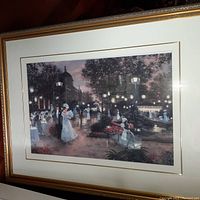 Framed artwork showing an elegant outdoor wedding scene with bride and groom dancing, guests, and an ornate gold frame.