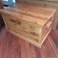 Closed view of wooden chest showing light-colored thick wood, natural grain, block handles on sides.