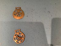 Two small brass dog bowl markers with cutout designs shown on grey surface