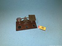 Small brass balance scale mounted on a wooden base with three circular indentations. No weights included.