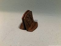 Pair of reddish-brown cast iron bookends joined together showing the raised design of two figures on each bookend.