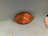 Oval copper pan with two handles placed on a blue surface