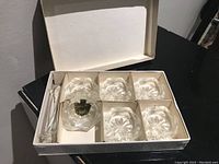Set of six small crystal glasses with decorative starburst pattern on bases shown inside original box. Two glass stirrers included.