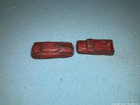 Top down view of two red old toy cars showing shape and paint wear.