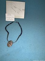 Silver necklace with dark round beads and large oval textured pendant, accompanied by matching silver earrings and signed authenticity cards.