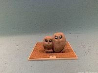 Front view of two soap stone owl figurines displayed on a square tile with cork insert.