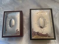 Two Italian jewelry boxes side by side showing velvet and faux leather exteriors with sterling silver lids featuring ornate floral embossed designs and central oval shapes.