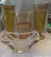 Photo showing all four vases together on a light surface including clear signed Daum vase at front and two tall gold vases and one peach vase in the back