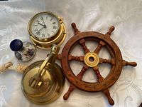 Photo showing all four pieces: brass bell with rope, wooden ships wheel, quartz ships clock with brass casing, and miniature Pussers rum decanter.