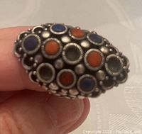 Close-up of one sterling silver ring with multiple stone inlays in blue and orange with decorative silver bead detailing.