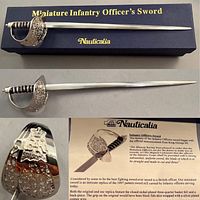Miniature Infantry Officer's Sword lying on and above its labeled box, showing the polished blade and metal basket hilt with intricate engravings.