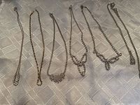 Six rhinestone necklaces laid out on a cloth surface, showing various designs and metal tones.