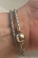 Close-up of the silver clasp engraved with PANDORA on the pale blue braided leather bracelet on wrist