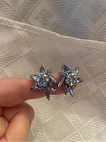 Close-up of Sherman Aurora Borealis clip-on earrings showing multi-faceted iridescent stones in floral star-shaped design with silver settings