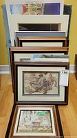 Stack of framed art prints and posters from 5x7 to 8x10 inches laid on floor showing brown wood frames with cream matting, illustrating vintage scenes and characters.