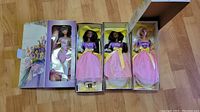 Four Barbie dolls in original boxes laid out, showing the purple and pink clothing and one doll with yellow hat.