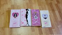 Four Barbie dolls in original Valentine-themed boxes laid flat on floor, showing front of boxes with visible branding and designs.