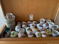 Overall view of assorted fine china cups and saucers with floral patterns and gold trims in display cabinet