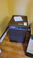 Mastercraft D20 dehumidifier placed on wooden floor in a corner, showing upright unit with cloth on top.