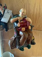 Front angle view showing the elderly man sitting in a rocking chair holding a red toy train and a bird on his hand