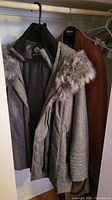 Grey Point Zero women's coat with fur trim hanging on left and brown leather coat on right