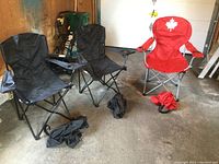 Three folding camp chairs: two black and one red with Canadian maple leaf emblem, all with armrests and cup holders, displayed in a garage environment