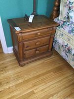 Pair of wooden night stands with 3 drawers each, medium wood tone, placed beside floral-patterned bed.