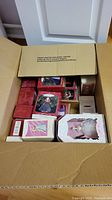 Open box filled with Hallmark Keepsake ornaments in original packaging, assorted styles visible with red color dominant.